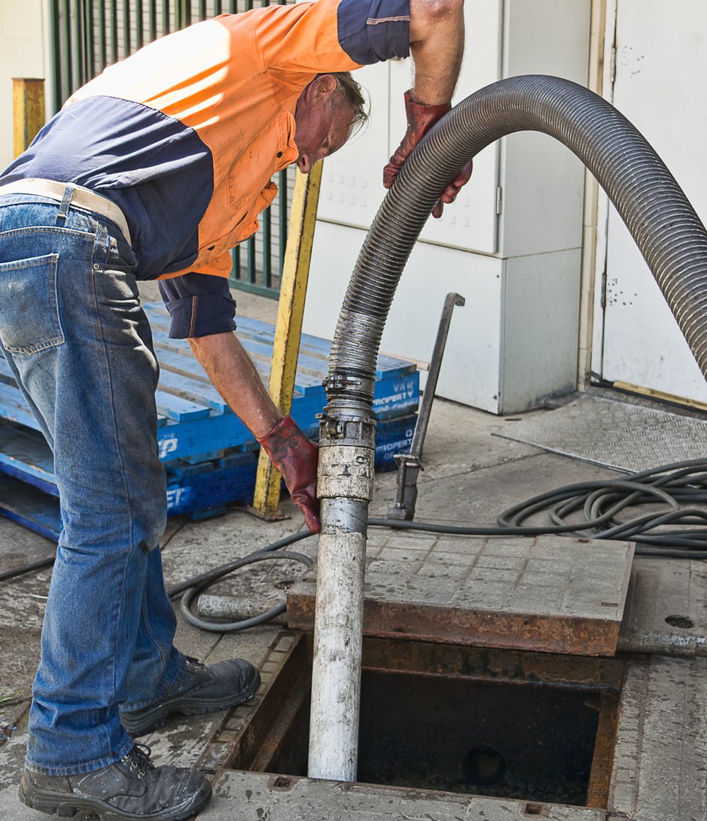 Pump-It operator guiding a vacuum hose into a grease trap