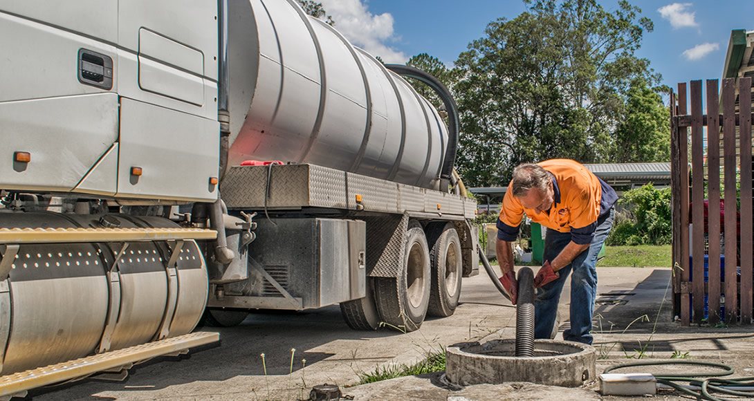 Pump-It operator feeding a vacuum hose into a septic tank beside the tanker on a residential property